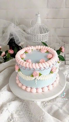 a three layer cake with pink and blue icing on a white platter next to flowers