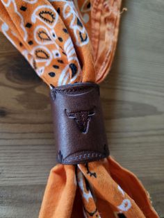 an orange and white patterned scarf with a brown leather cuff on it's end