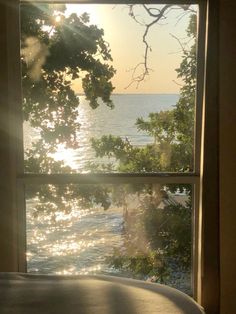 the sun is shining through an open window overlooking the water and tree branches in the foreground