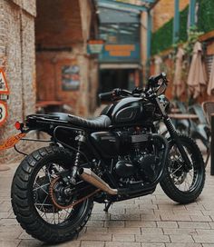 a black motorcycle parked in front of a building on a brick sidewalk next to tables and chairs