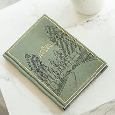 a green book sitting on top of a white table next to a cup and saucer