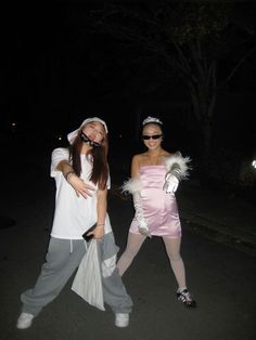 two women dressed up in costumes standing next to each other on the street at night