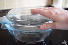 a person's hand on top of a glass casserole dish with lid