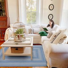 a woman sitting on a white couch in a living room with a birdcage