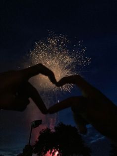 two hands making a heart shape with fireworks in the background