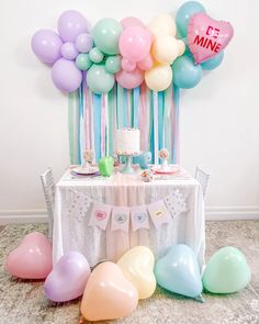 a table topped with balloons and cake next to a white table cloth covered in pastel colors