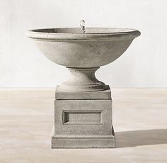 a concrete fountain with a water spout on the top and a light colored wall in the background