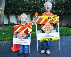 two young boys standing next to each other holding construction signs with caution written on them