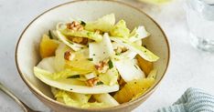 a bowl filled with lettuce, apples and walnuts next to a glass of water