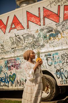 a woman is standing in front of a van with graffiti on it and holding flowers