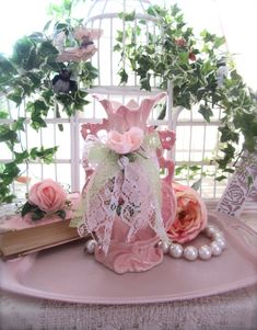 a pink vase sitting on top of a table next to pearls and flowers in front of a birdcage