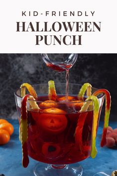 a halloween punch is being poured into a glass with oranges and candy on the rim