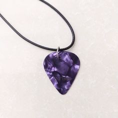 a necklace with a purple heart shaped pendant on a black cord hanging from it's side