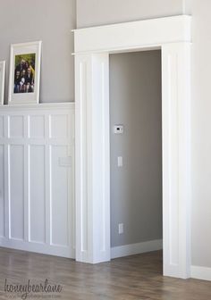 an empty room with white paneling and pictures on the wall above it, in front of a fireplace