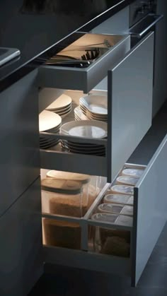 an open drawer in a kitchen with plates and utensils on the bottom shelf