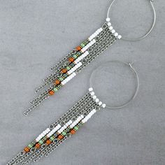 a pair of silver and orange beaded bracelets on a gray surface with hoop earrings