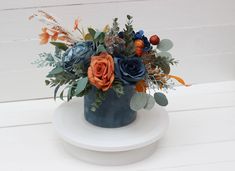 an arrangement of flowers in a blue vase on a white plate with wood planks