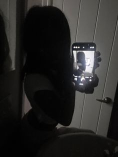 a person holding up a cell phone to take a selfie in the bathroom at night