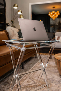 an apple laptop sitting on top of a clear table in a living room with couches