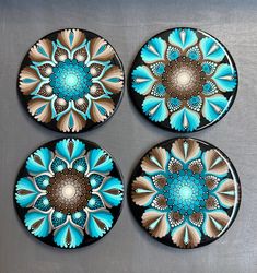 four plates with blue and brown designs are on a silver surface, one is circular