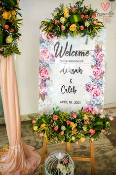 a welcome sign with flowers and greenery on it next to a birdcage