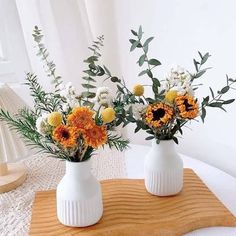 two white vases with yellow and white flowers in them