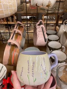 a hand holding a coffee mug in front of many other cups and bowls on display