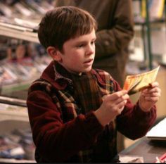 a young boy standing in front of a pile of magazines