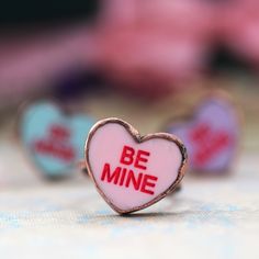 a pink heart shaped ring with the words be mine written in red on it's center