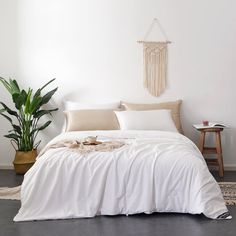 a bed with white sheets and pillows in a room next to a potted plant