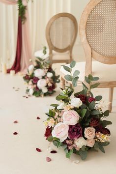 flowers and greenery are arranged on the floor in front of chairs with petals scattered around them