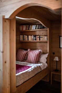 a bed with bookshelves and pillows in a room that has wood paneling on the walls