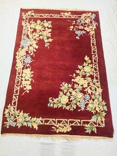 a red area rug with flowers and vines on the border is laying on a white surface