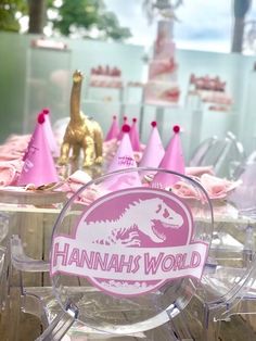 pink party hats are set up on clear acrylic chairs for a dinosaur themed birthday