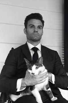 a man in a suit holding a cat while sitting on his lap and looking at the camera