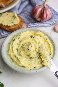 a bowl of hummus with garlic and bread in the background