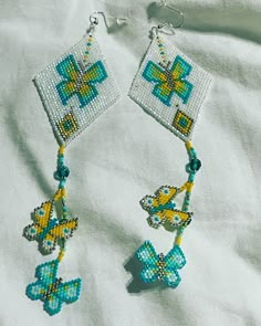 a pair of blue and yellow beaded earrings sitting on top of a white sheet