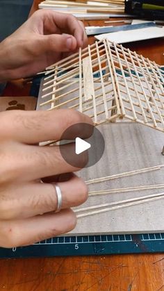 two hands are working on a wooden structure that is being made out of wood sticks