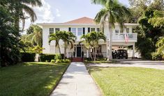 a large white house with palm trees in the front yard and walkway leading to it