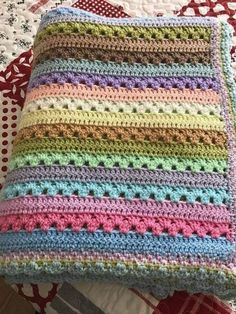 a multicolored crocheted blanket sitting on top of a bed next to a pillow