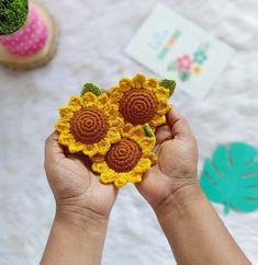 someone is holding two crocheted sunflowers in their hands