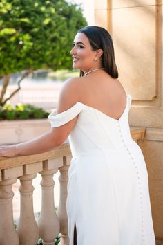 a woman in a white dress standing on a balcony with her hand on the railing