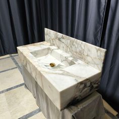 a white marble sink sitting on top of a tiled floor next to a black curtain