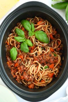 a black bowl filled with spaghetti and basil