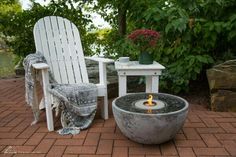 a white chair sitting on top of a brick patio next to a fire pit with a lit candle in it