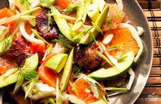 a plate filled with sliced oranges, avocado and other food on top of a table