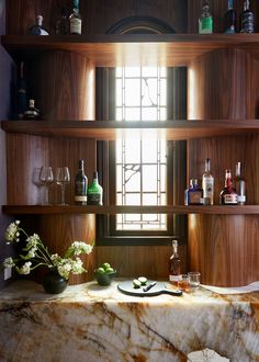 a marble counter top sitting under a window next to shelves filled with bottles and glasses