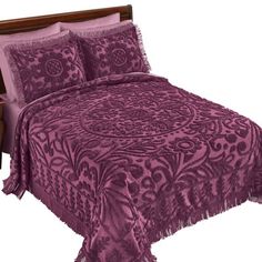 a bed with purple bedspread and pillows on top of the headboard in front of a night stand