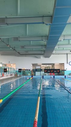 an indoor swimming pool with blue tiles and green poles on the side, people are in the background