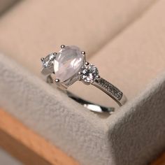 an engagement ring in a box with diamonds on the sides and a large white stone surrounded by smaller round stones